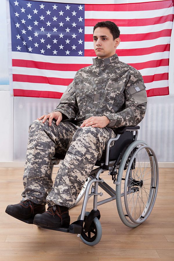 man wearing military clothing in wheelchair in front of American flag